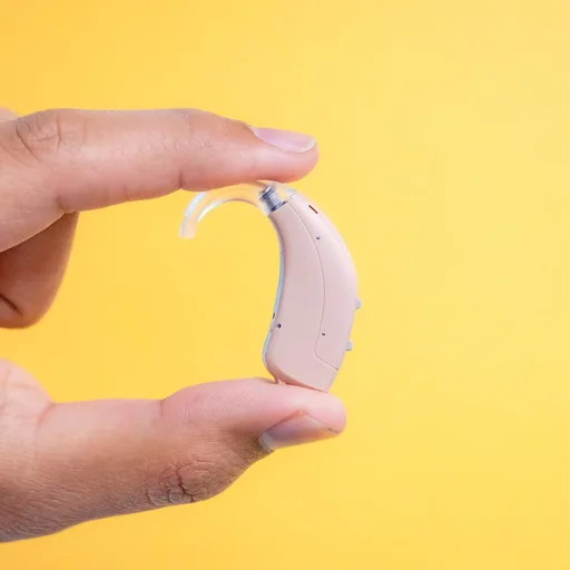 Close-up of a hand holding a hearing aid between two fingers, illustrating product care and warranty coverage.